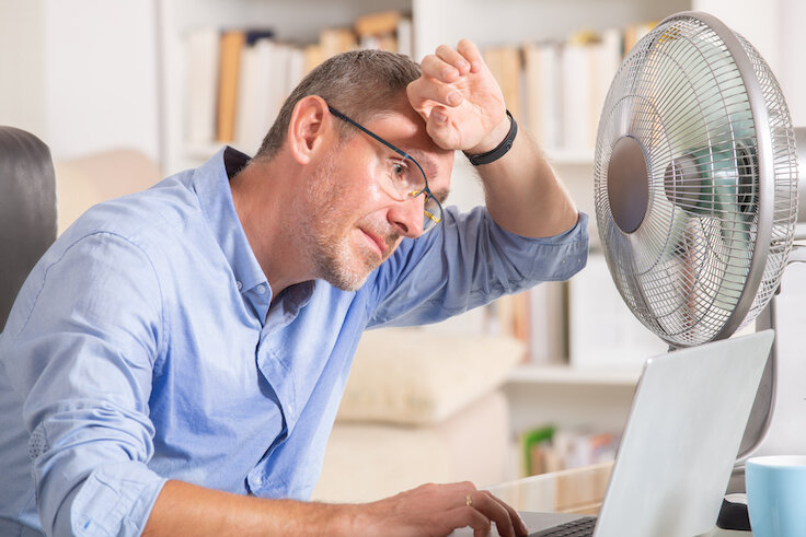 man cooling off with electric fan at desk